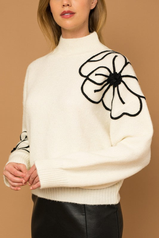 Flower Embroidery Mock Neck Sweater. white knit sweater with large black embroidered flowers.