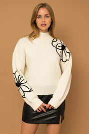 Flower Embroidery Mock Neck Sweater. White knit sweater with large black embroidered flowers.